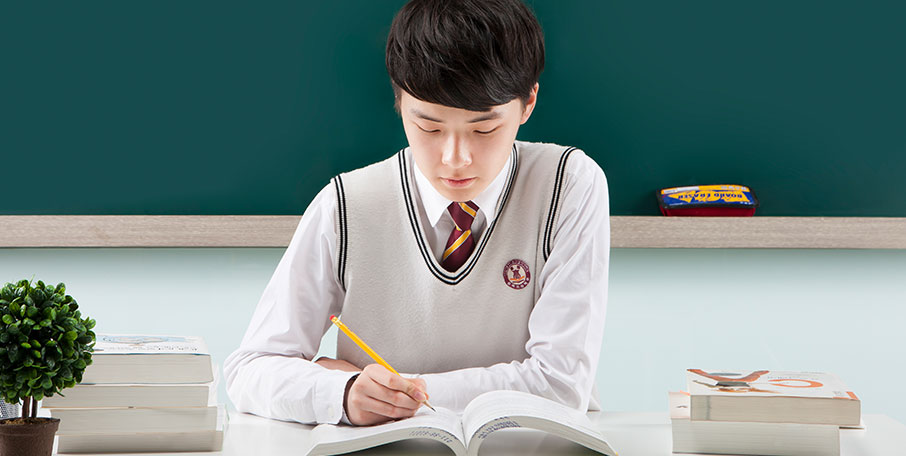 CLP Class 이미지 칠판을 배경으로 한 학생이 책상에 앉아 연필을 쥔 채 책을 보고 있다.